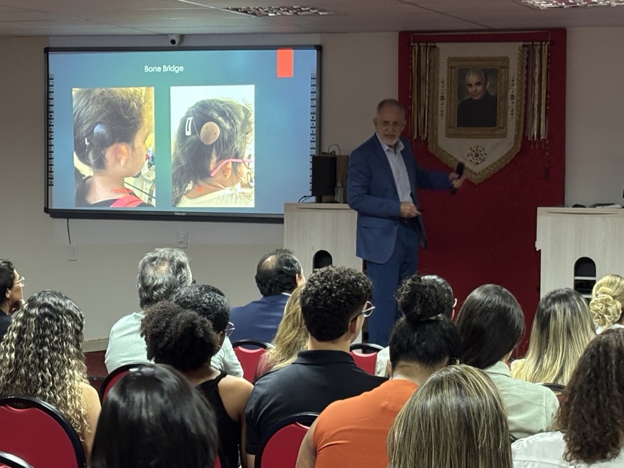 Palestrante conduzindo aula científica, com slide projetado, diante de plateia